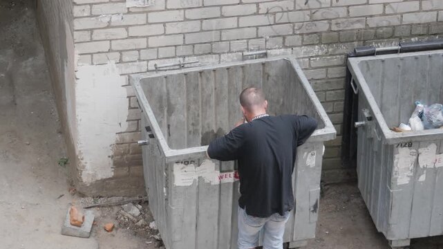 Man Looking Food In Trash Can. Back View
