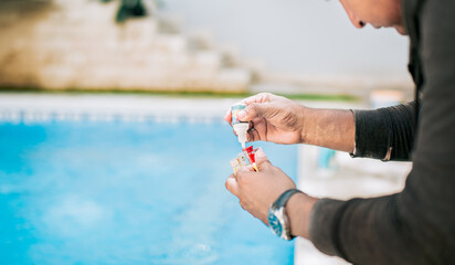 Man using tester kit to measure chlorine and ph in swimming pools. Person testing the PH of the...