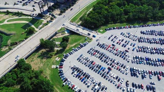 Parking lot near main boulevard street, lush greenery trees, full of electric and gas cars parked on parallel pattern with pavement marking, parking management in metropolitan urban area, aerial