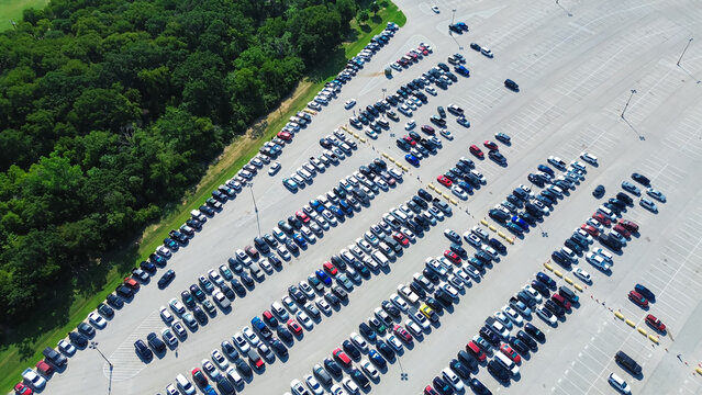 Lush greenery trees near busy dense parking lots full of electric and gas vehicles, parallel pattern and pavement marking number, parking management in metropolitan urban area, aerial view, Texas