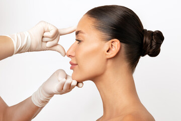 Plastic surgery and beauty concept. Profile shot of woman consulting before rhinoplasty operation, surgeon touching woman nose, white background, side view