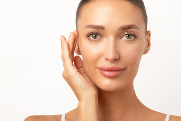 Aesthetic procedures concept. Portrait of young European woman touching glowing skin, white studio...