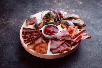 Snacks on wooden utensils. Sliced bacon and hunting sausages. Small snacks for beer in the form of fish on bread. Food on a dark texture background.