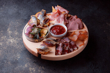 Snacks on wooden utensils. Sliced bacon and hunting sausages. Small snacks for beer in the form of fish on bread. Food on a dark texture background.