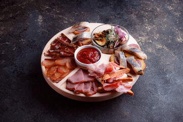 Snacks on wooden utensils. Sliced bacon and hunting sausages. Small snacks for beer in the form of fish on bread. Food on a dark texture background.