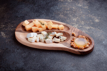 Cheese cut into pieces on a wooden board. Serving cheeses with honey and nuts. The concept of a healthy lunch of hard cheese and dor blue. Dishes for serving banquets and special occasions.