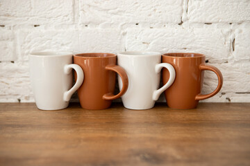 brown and white cups stand on a wooden table near a white wall