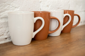 brown and white cups stand on a wooden table near a white wall