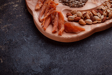 Snacks for beer on wooden utensils. Sliced dried fish in pieces and in the form of sticks. Mix of nuts and cheeses. Food on a dark texture background. Eco-friendly tableware.