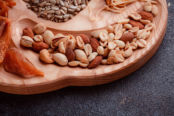 Snacks for beer on wooden utensils. Sliced dried fish in pieces and in the form of sticks. Mix of nuts and cheeses. Food on a dark texture background. Eco-friendly tableware.