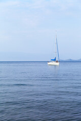 Fototapeta premium Summer vacation on Baikal Lake. A tourist girl is relaxing on a pleasure sailing yacht and taking pictures of a beautiful seascape with Olkhon Island in the distance on her mobile phone