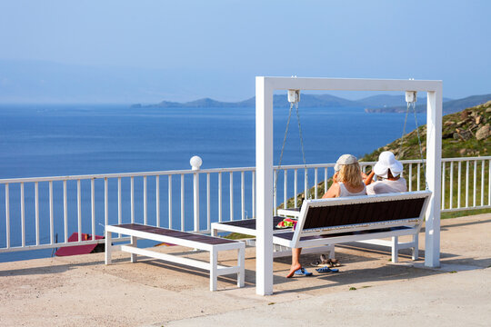 Baikal Lake in summer. Two girls are relaxing on the high bank of the Small Sea, swinging on a swing, eating a watermelon and admiring the seascape on a sunny day in August