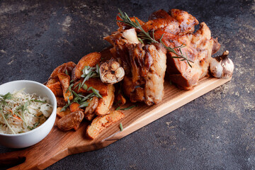 A set dish: a large fried piece of meat on the bone, country-style grilled potatoes, a mini salad of cabbage, bean sprouts, chia seeds and green onions. Original serving on a wooden cutting board.