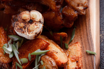 A set dish: a large fried piece of meat on the bone, country-style grilled potatoes, a mini salad of cabbage, bean sprouts, chia seeds and green onions. Original serving on a wooden cutting board.