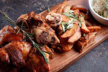 A set dish: a large fried piece of meat on the bone, country-style grilled potatoes, a mini salad of cabbage, bean sprouts, chia seeds and green onions. Original serving on a wooden cutting board.