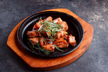 Hot frying pan with pieces of fried meat in caramelized sauce. Cooked and fresh vegetables as garnish and garnish.