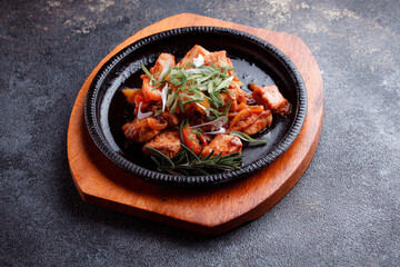 Hot frying pan with pieces of fried meat in caramelized sauce. Cooked and fresh vegetables as garnish and garnish.