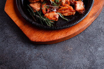 Hot frying pan with pieces of fried meat in caramelized sauce. Cooked and fresh vegetables as garnish and garnish.