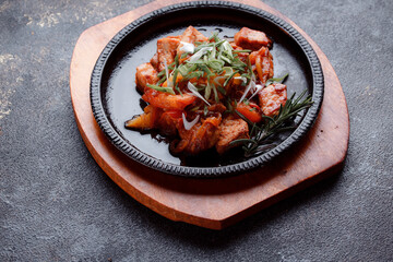Hot frying pan with pieces of fried meat in caramelized sauce. Cooked and fresh vegetables as garnish and garnish.
