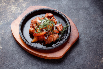 Hot frying pan with pieces of fried meat in caramelized sauce. Cooked and fresh vegetables as garnish and garnish.