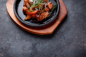 Hot frying pan with pieces of fried meat in caramelized sauce. Cooked and fresh vegetables as garnish and garnish.