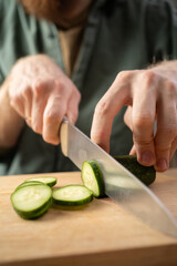 close-up of male hands with kitchen knife cutting fresh cucumber for salad