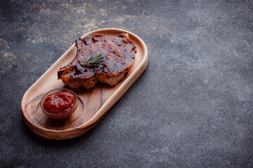 Grilled pork steak in caramelized sauce. Serving meat on eco-friendly wooden utensils. A sprig of fresh rosemary and tomato sauce.