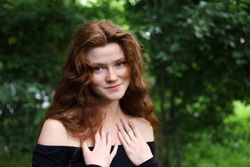Naklejka premium Portrait of smiling ginger girl with long red hair and freckles standing in summer park. Young sensual model, natural female beauty