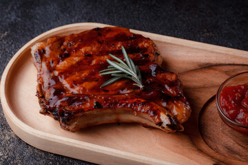 Grilled pork steak in caramelized sauce. Serving meat on eco-friendly wooden utensils. A sprig of fresh rosemary and tomato sauce.