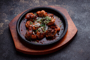 Hot frying pan with pieces of fried meat in caramelized sauce. Cooked and fresh vegetables as garnish and garnish.  A dish with the addition of flax seeds and sesame seeds.
