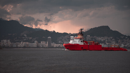 A large red offshore supply vessel navigates through the waters near Rio de Janeiro, with the...