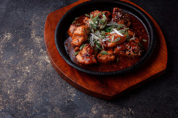 Hot frying pan with pieces of fried meat in caramelized sauce. Cooked and fresh vegetables as garnish and garnish.  A dish with the addition of flax seeds and sesame seeds.