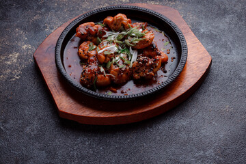 Hot frying pan with pieces of fried meat in caramelized sauce. Cooked and fresh vegetables as garnish and garnish.  A dish with the addition of flax seeds and sesame seeds.