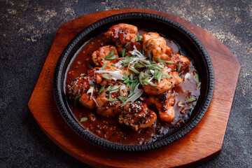 Hot frying pan with pieces of fried meat in caramelized sauce. Cooked and fresh vegetables as garnish and garnish.  A dish with the addition of flax seeds and sesame seeds.