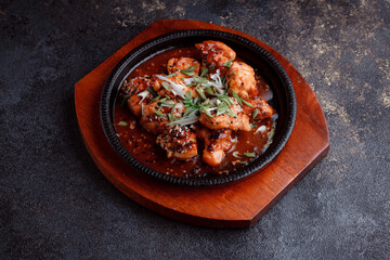 Hot frying pan with pieces of fried meat in caramelized sauce. Cooked and fresh vegetables as garnish and garnish.  A dish with the addition of flax seeds and sesame seeds.
