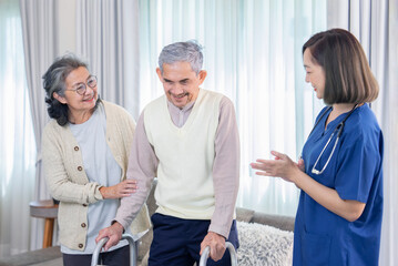 old asian man patient trying to walk by using walker,being assist by a nurse caregiver and a senior wife standing and supporting beside him,concept of elderly health care,homecare,home health nursing