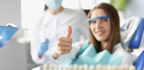 A woman at the dentist shows a thumbs up gesture, blurry, close-up. Professional dental care,...