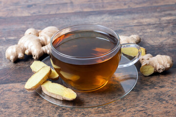 Ginger tea in transparent tea cup on wooden table, sliced ginger and root as decoration around.