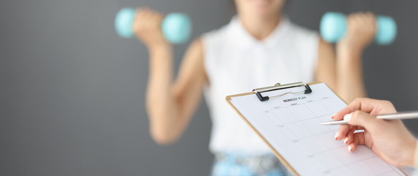 Female hands are writing down a workout plan, close-up, blurry. Fitness trainer control, exercises with dumbbells
