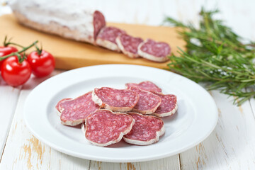 traditional Spanish salami fuet sausage or dry sausage cut in slices on a white ceramic plate, isolated on a kitchen table.