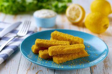 Tasty crispy deep fried fish fingers served with lemon and tartar sauce on wooden table.