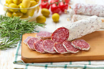 traditional Spanish salami fuet sausage with spices and herbs on a cutting board close up.