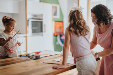 Young mother engaging in creative activities by drawing and painting with her little daughters at home. Family bonding through art and creativity.