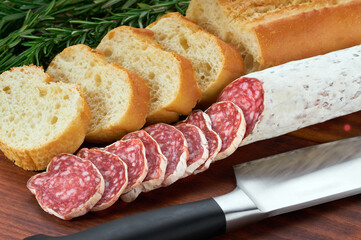 traditional Spanish salami fuet sausage with rosemary and baguet  on a cutting board close up.