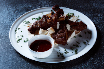 A large piece of spicy grilled meat. Ribs fried to a crisp with spices and herbs. Restaurant serving dishes with sauce and micro-herbs.