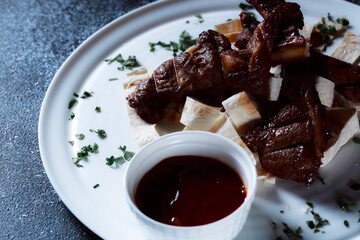 A large piece of spicy grilled meat. Ribs fried to a crisp with spices and herbs. Restaurant serving dishes with sauce and micro-herbs.