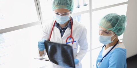Two female doctors in the clinic are looking at an x-ray of the lungs, close-up. Diagnosis of...