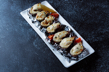 Boiled oysters with melted cheese. Nice serving of oysters on a large white platter. Seafood prepared for a restaurant on a dark blue background.