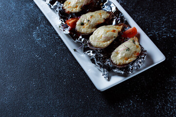 Boiled oysters with melted cheese. Nice serving of oysters on a large white platter. Seafood prepared for a restaurant on a dark blue background.