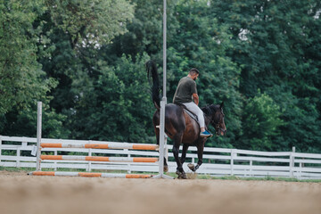 Man riding a horse in an outdoor riding arena with a photographer capturing the moment. Countryside setting with a white fence and lush greenery in the background.